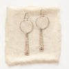 The pakal long triangle hoop earrings styled on tan linen