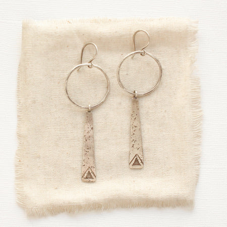 The pakal long triangle hoop earrings styled on tan linen