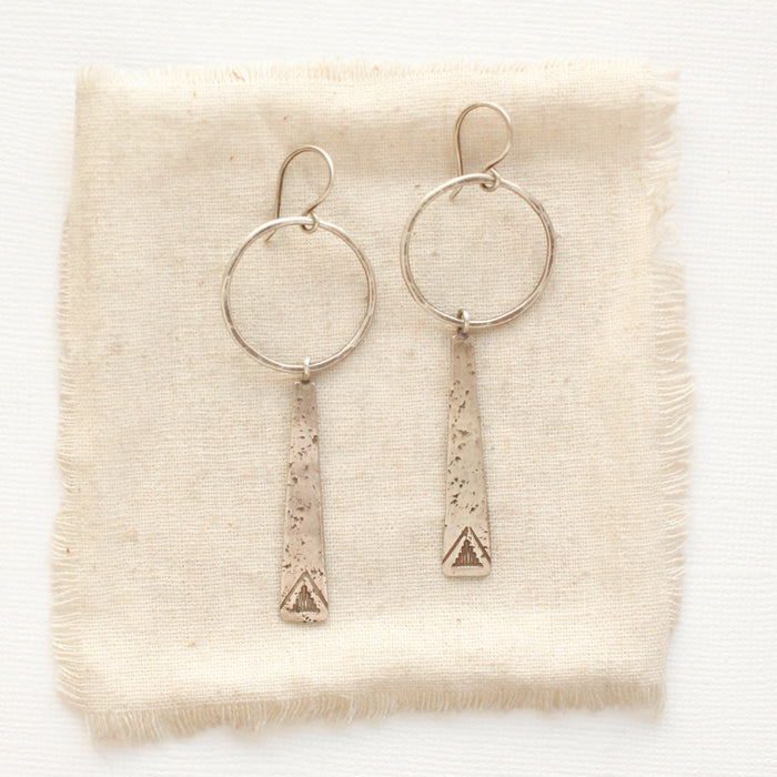 The pakal long triangle hoop earrings styled on tan linen