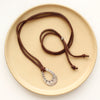 The pakal teardrop adjustable leather necklace styled on a tan plate to show the entire leather necklace and silver slider