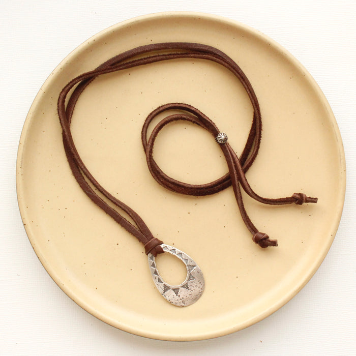 The pakal teardrop adjustable leather necklace styled on a tan plate to show the entire leather necklace and silver slider