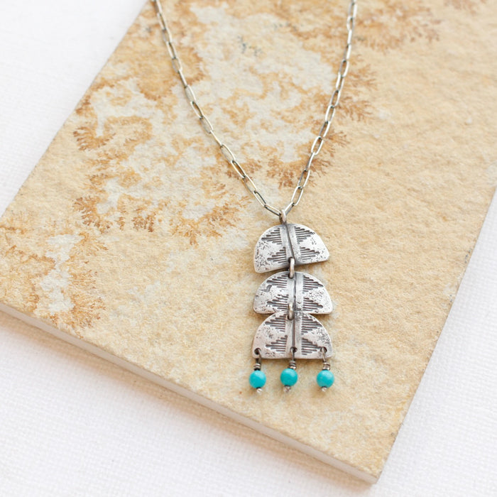The pakal trio turquoise dangle necklace styled on a tan rock