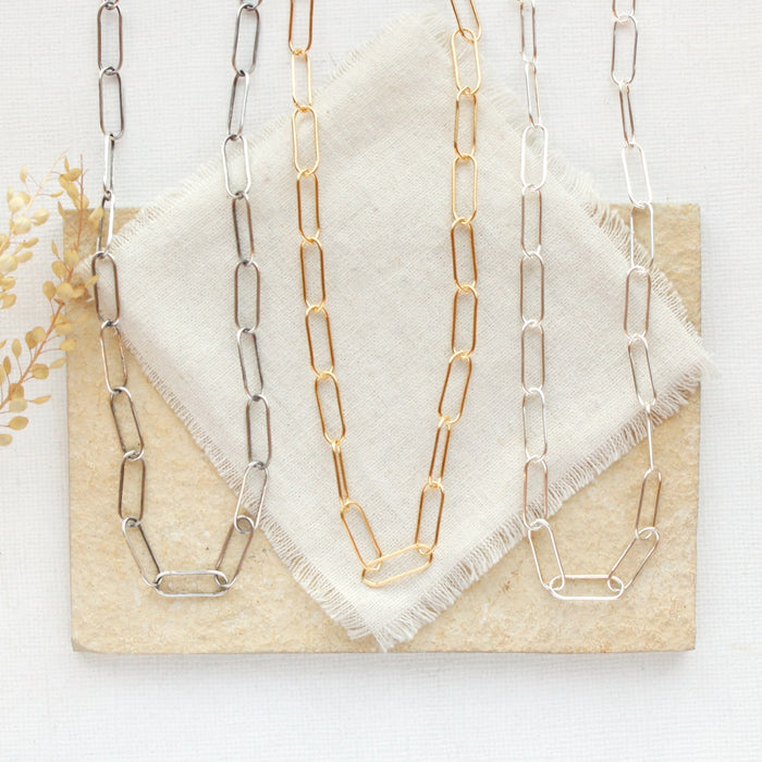 All three options of the paperclip necklace styled on a tan rock with linen and dried grass