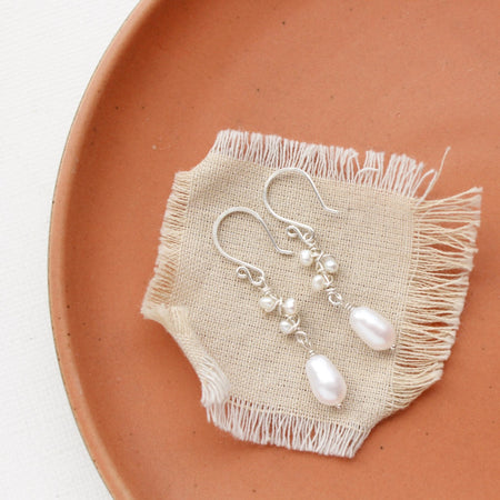 The pearl bud vine earrings styled on an orange plate with linen 