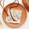 The pearl columbine hoop earrings styled on an orange plate with the matching leather necklace