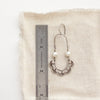 A pearl columbine hoop earring next to a ruler for size reference