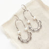 The pearl columbine hoop earrings styled on tan linen