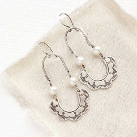 The pearl columbine hoop earrings styled on tan linen