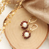 The pearl and garnet flower earrings styled on wood with brown velvet and dried grass
