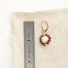 A pearl and garnet flower earring next to a ruler for size reference