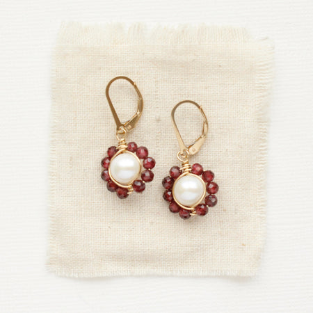 The pearl and garnet flower earrings styled on tan linen