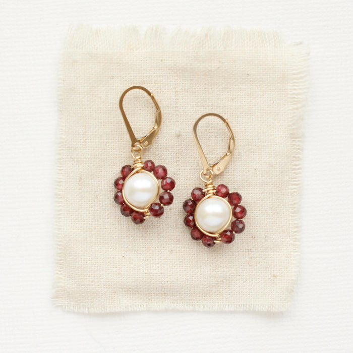 The pearl and garnet flower earrings styled on tan linen