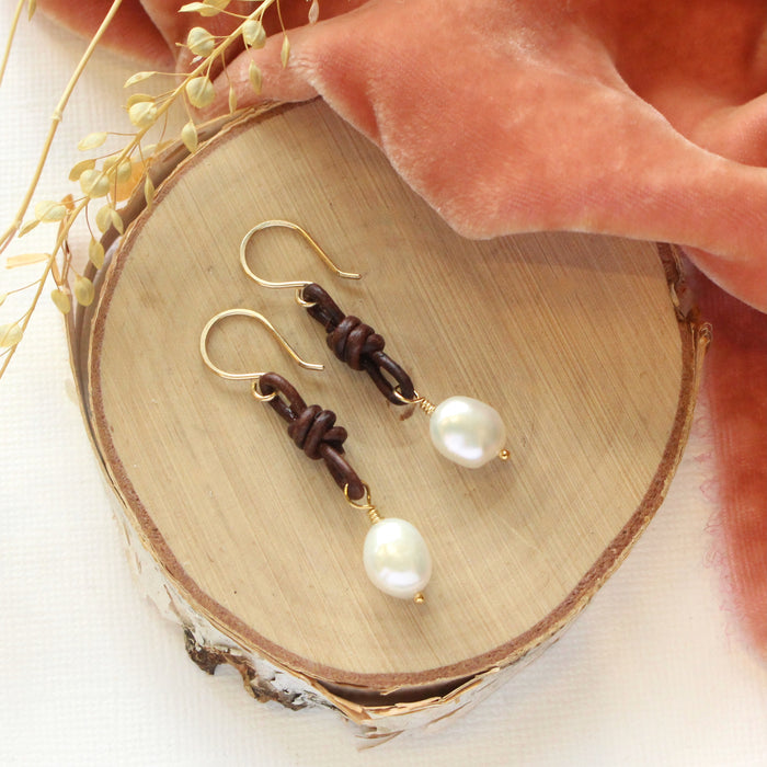 The pearl and leather earrings styled on wood with orange velvet and dried grass