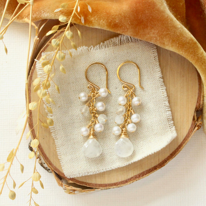 The pearl and moonstone fringe earrings styled on wood with yellow velvet and dried grass