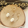 The carved pearl skull hoop earrings styled on wood with gray velvet and dried grass