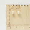 The carved pearl skull hoop earrings on a wooden ruler for size reference