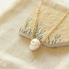 The carved pearl skull necklace styled on a tan rock and tan linen