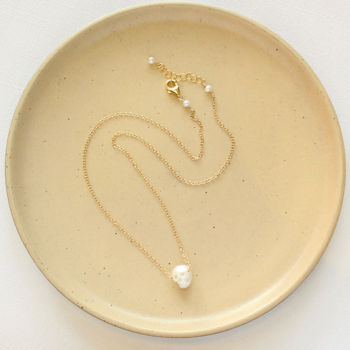 The carved pearl skull necklace styled on a tan plate to show the adjustable lobster clasp closure