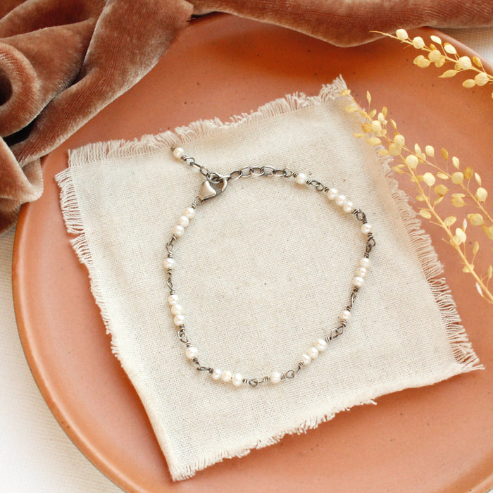 The wrapped pearl bracelet styled on a orange plate with tan linen, orange velvet, and dried grass