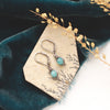The wrapped amazonite earrings styled on a tan rock with blue velvet and dried grass