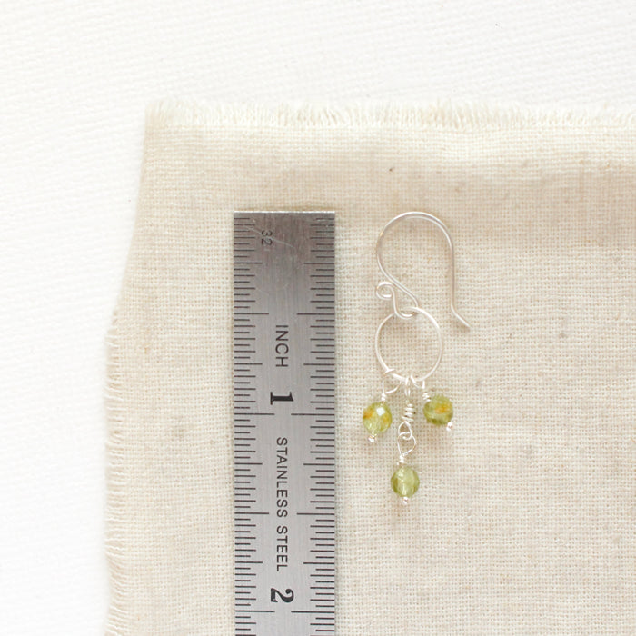 A peridot trio hoop earring next to a ruler for size reference