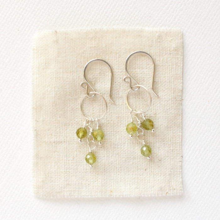 The peridot trio hoop earrings styled on tan linen