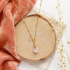 The morganite drop necklace styled on wood with orange velvet and dried grass