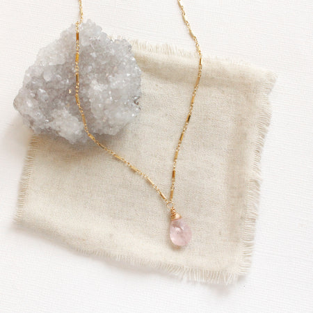 The morganite drop necklace styled on a tan linen with a gray crystal