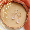 The morganite drop earrings styled on wood with orange velvet and dried grass