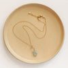 The pinned aquamarine gold necklace styled on a tan plate to show the adjustable lobster clasp closure