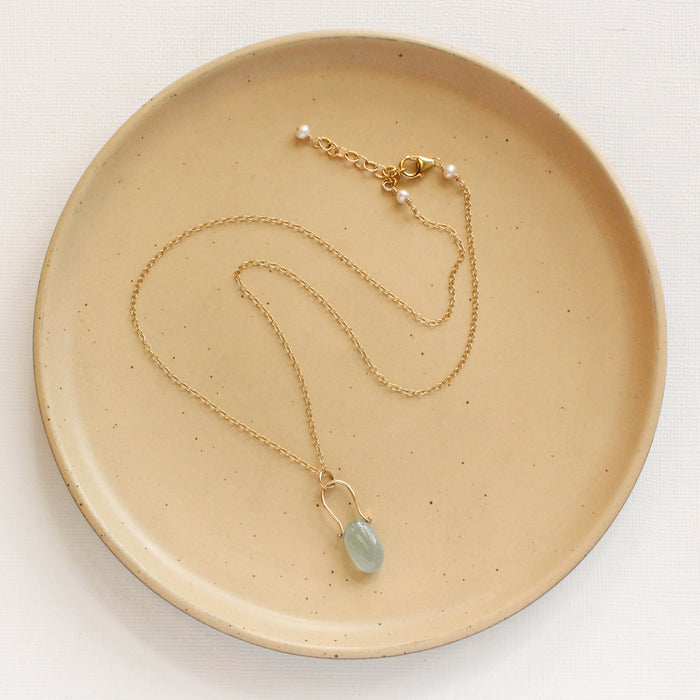 The pinned aquamarine gold necklace styled on a tan plate to show the adjustable lobster clasp closure