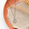 The pinned columbine disc necklace styled on an orange plate with linen and dried grass