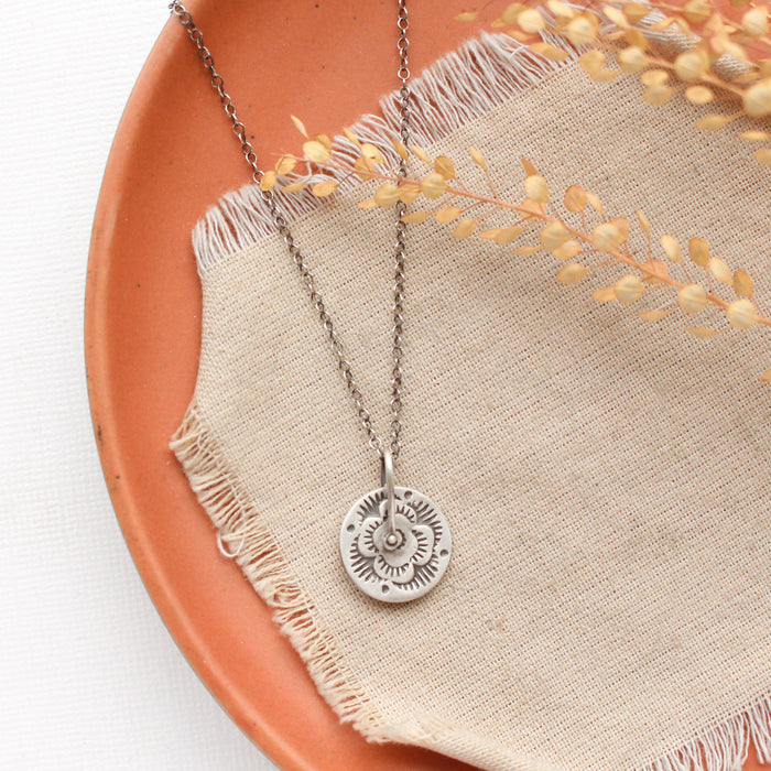 The pinned columbine disc necklace styled on an orange plate with linen and dried grass