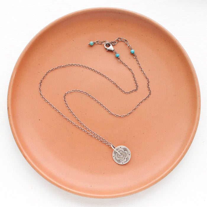 The pinned columbine disc necklace styled on an orange plate to show the adjustable lobster clasp closure
