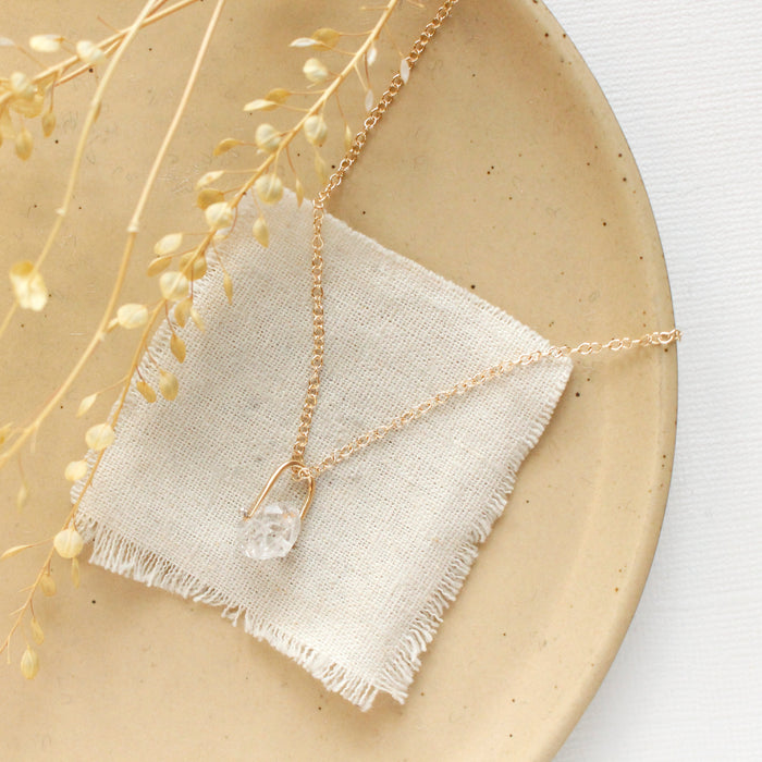 The pinned gold herkimer diamond necklace styled on a tan plate with linen and dried grass
