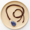 The pinned sodalite adjustable leather necklace styled on a tan plate to show the whole leather necklace and silver slider