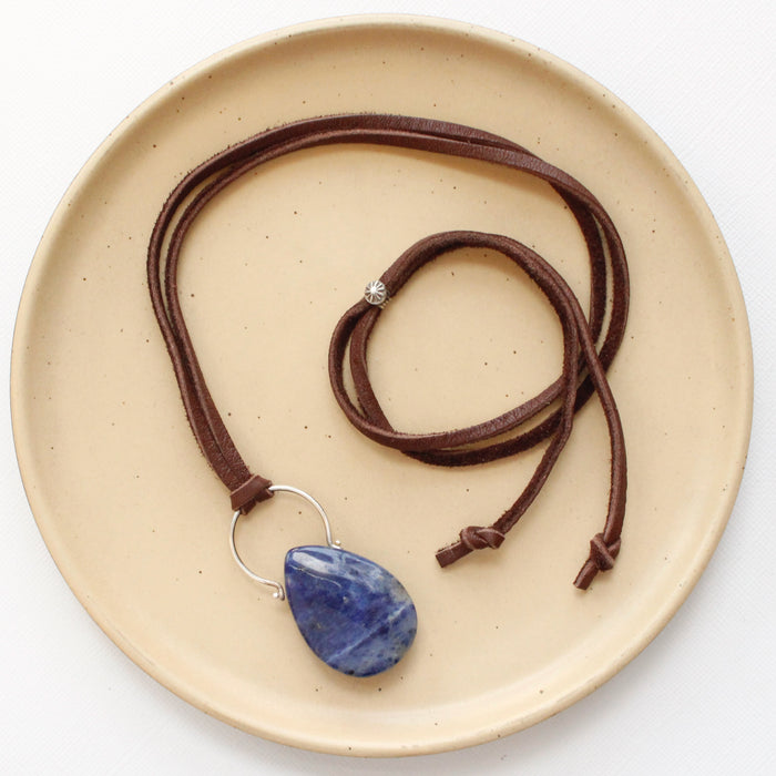 The pinned sodalite adjustable leather necklace styled on a tan plate to show the whole leather necklace and silver slider