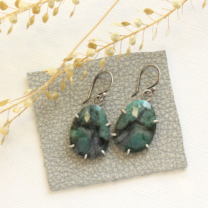 The prong set emerald earrings styled on gray leather with dried grass