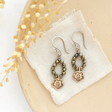The bronze mini cactus flower and pyrite earrings styled on a tan plate with linen and dried grass