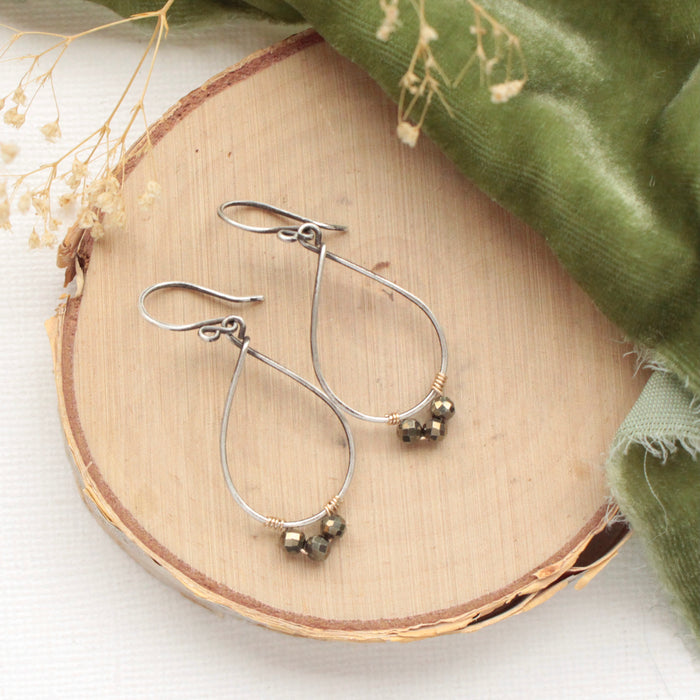 The pyrite wrapped teardrop hoop earrings styled on wood with green velvet and dried grass