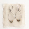 The pyrite teardrop hoop earrings styled on tan linen