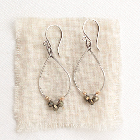 The pyrite teardrop hoop earrings styled on tan linen
