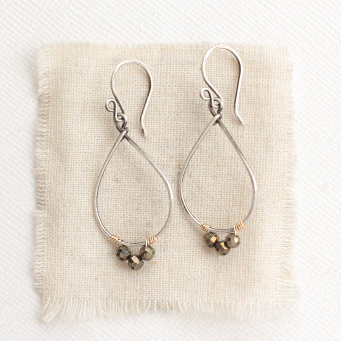 The pyrite teardrop hoop earrings styled on tan linen