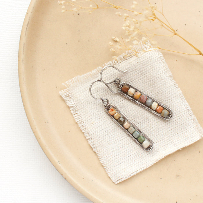 The rainbow agate beaded bar earrings styled on a tan plate with linen and dried grass