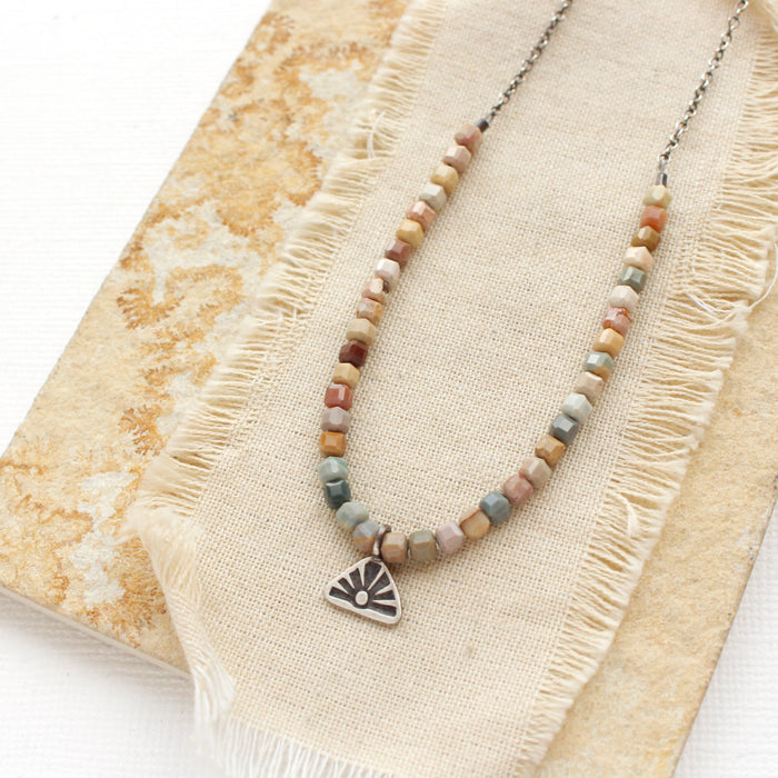 The rainbow agate sun rise charm necklace styled on a tan rock with linen