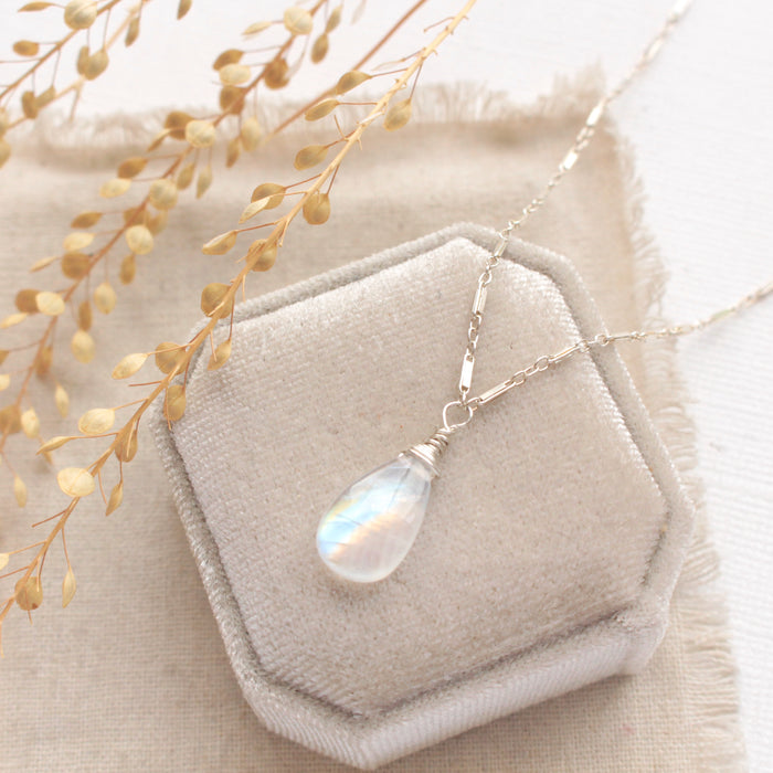 The rainbow moonstone silver bar necklace styled on a white velvet box with linen and dried grass