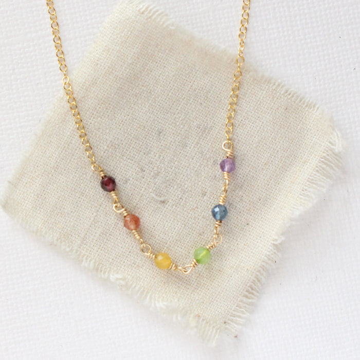 The wrapped gold rainbow necklace styled on tan linen