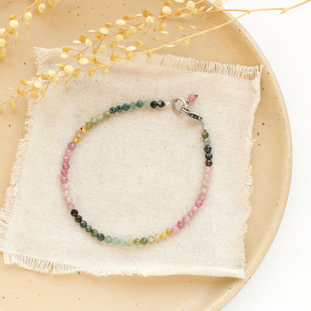 The rainbow tourmaline bracelet styled on a tan plate with linen and dried grass