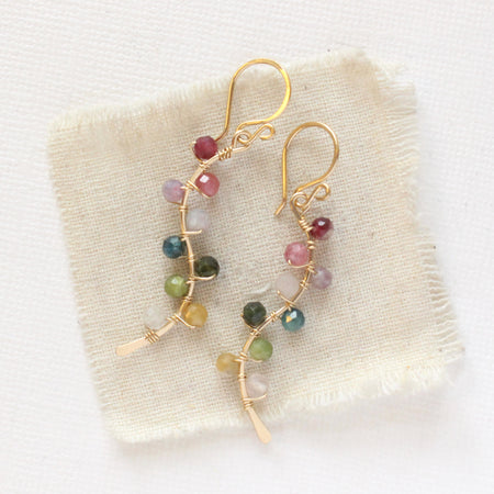 The rainbow vine earrings styled on tan linen