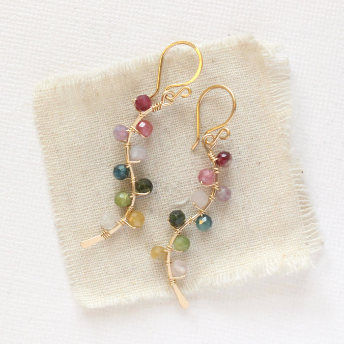 The rainbow vine earrings styled on tan linen